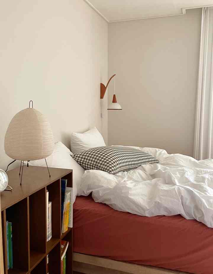 White and brown toned bedroom featuring gingham check pillow, wall sconce, and bookshelf creating a cozy ambiance