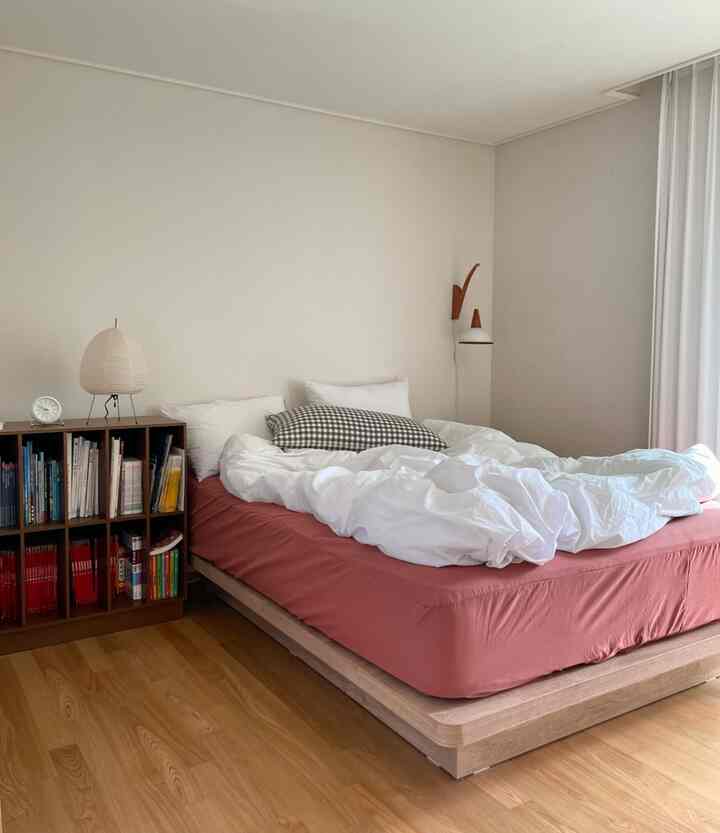 Natural brown floor and white curtains in a Mid-Century Modern style bedroom featuring a reddish mattress cover and bookshelf in a serene space
