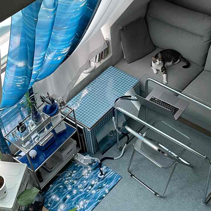 ブルーとグレーのトーンの小さなホームオフィス、猫のいるソファとガラスの机が配置された印象的な空間