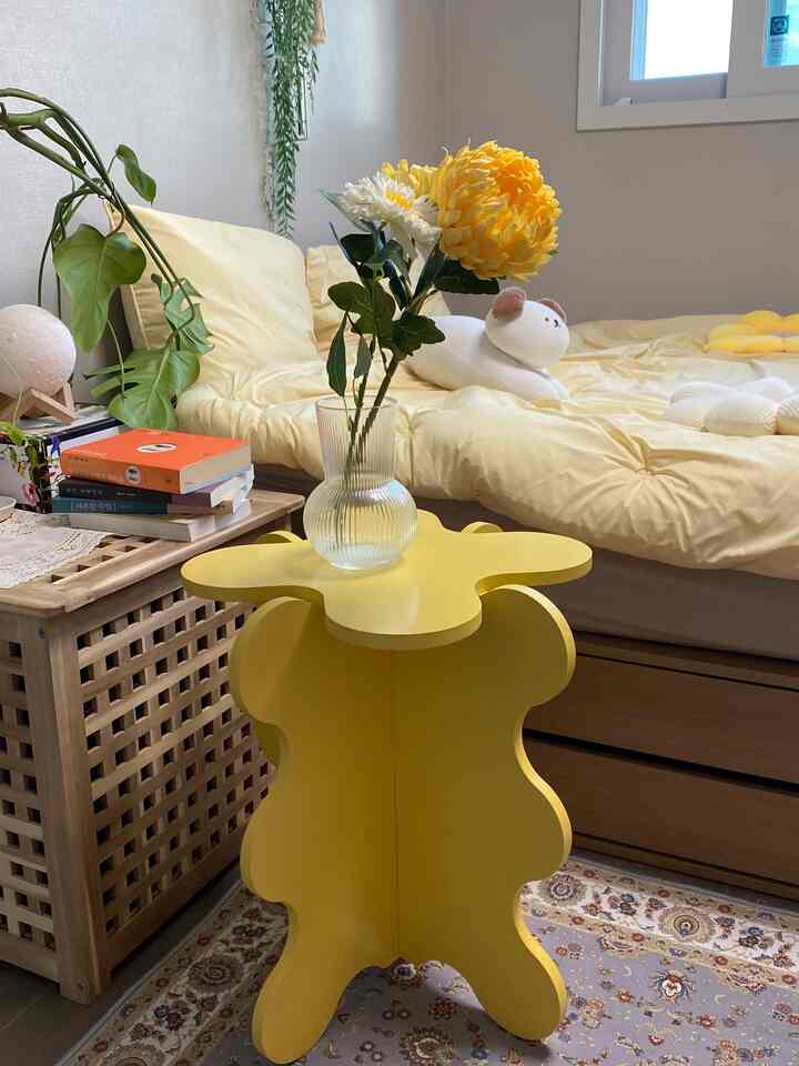 Bright yellow and natural wood tone bedroom featuring a flower-shaped yellow side table and plant decor, creating a cozy atmosphere