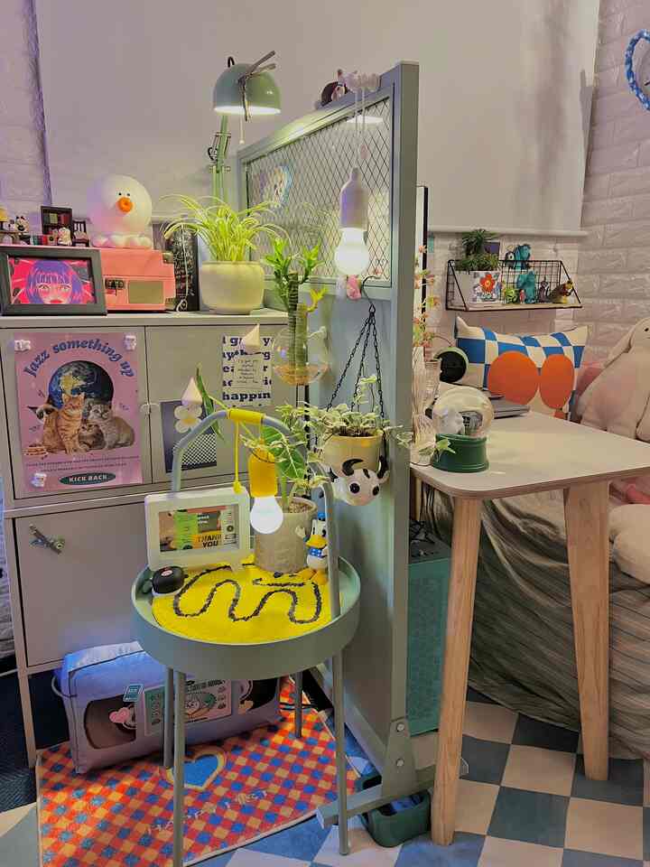 Light green and natural wood tone small room featuring plants, various decor items, and a cozy table with storage cabinet