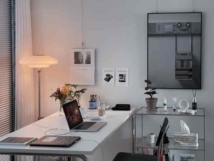White and gray toned home office space featuring a desk with laptop and floor lamp in a clean setup
