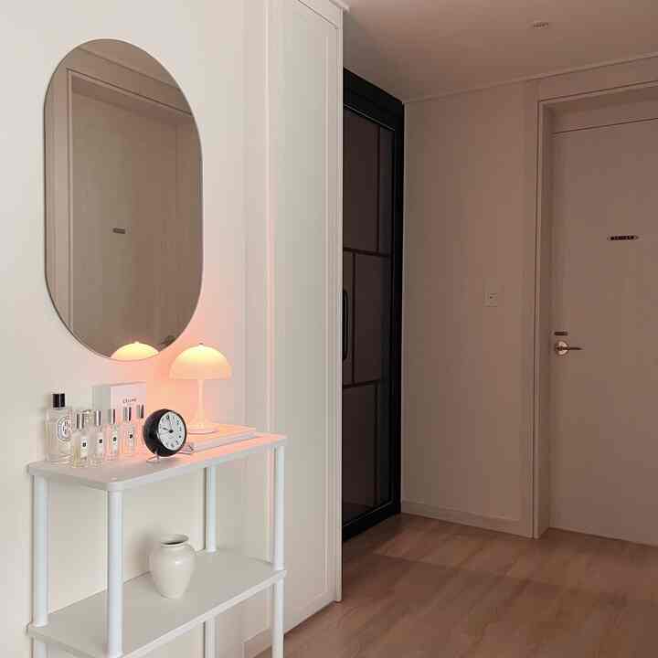 Simple living room entrance in white and natural wood tones, featuring a mirror and table lamp with a clean and bright atmosphere
