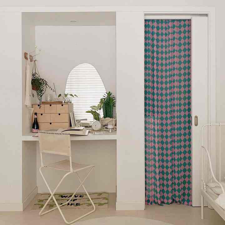 Beige-toned compact home office space with checkered chiffon curtain, desk, and plants creating a cozy interior