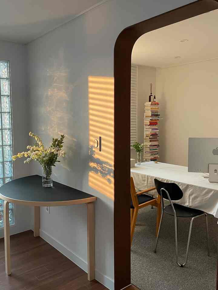 A white and wood-toned study and dining room featuring a simple layout with an Artek semi-circular table and Arno chairs