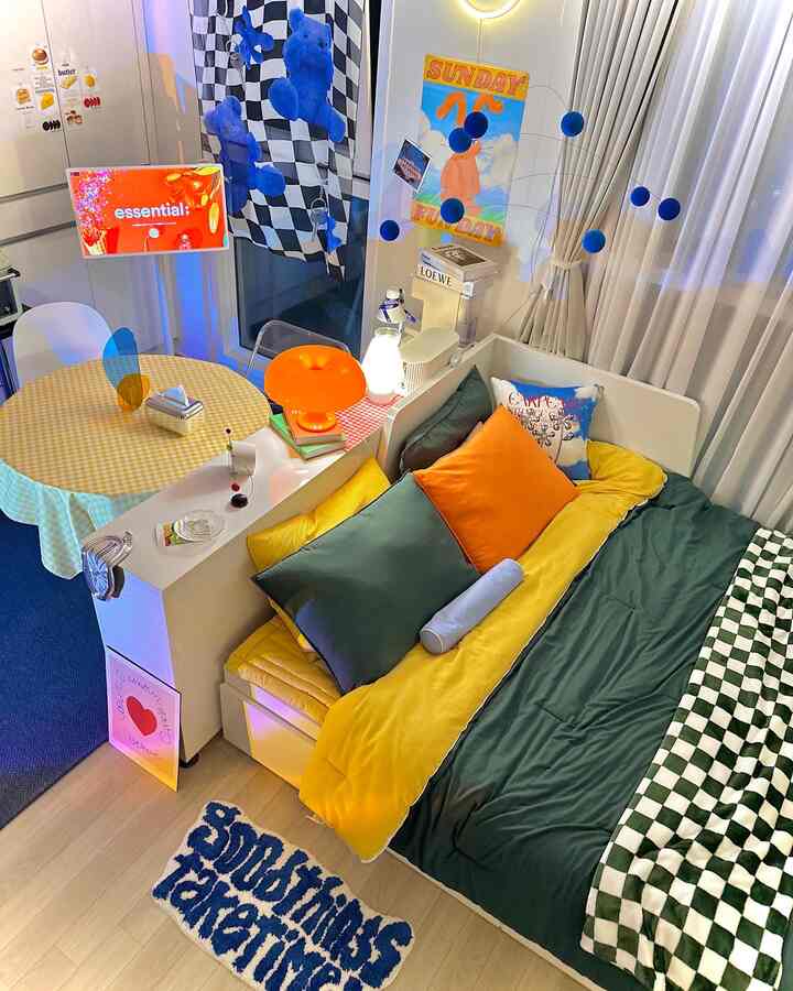 Bright bedroom with yellow and green bedding, orange chair and blue mobile, embodying a cozy mid-century modern aesthetic