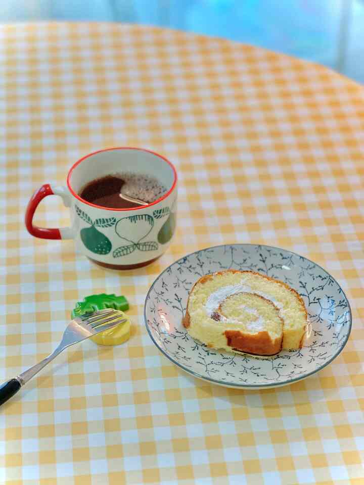 黄色のチェック柄テーブルクロスにレトロパターンのマグカップとクリームロールケーキが置かれた雰囲気のあるおうちカフェ