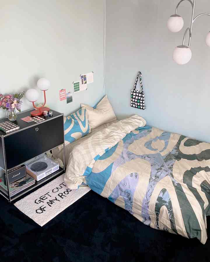 Soft blue and white toned single bedroom featuring simple black furniture and patterned bedding in a compact space