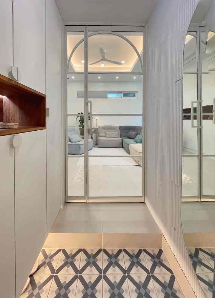 A modern, clean entrance in white and gray tones with glass door revealing a living room featuring a sofa