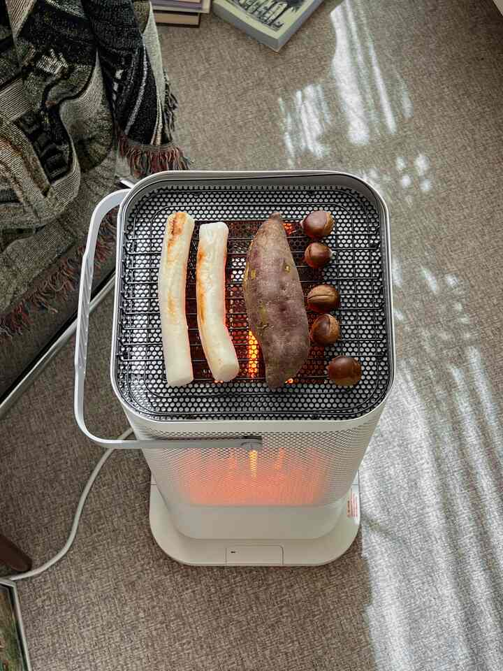 ナチュラルカラーの狭い部屋に、オバンヒーターでさつまいもと餅を焼いている雰囲気のある空間