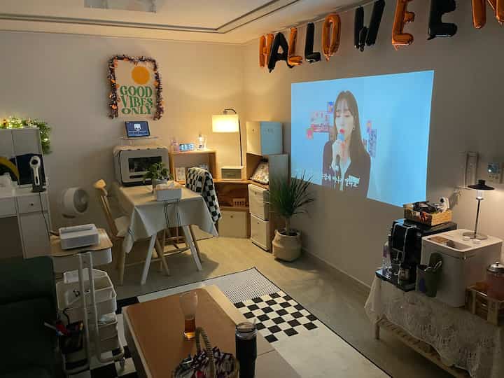 White and beige living room featuring a projector screen, beverage corner, and tables with chairs creating a cozy home party atmosphere