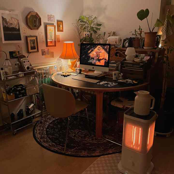 暖かいオレンジ色調と木製デスクが調和する、電気ヒーターと植物が配置された居心地の良いホームオフィス空間