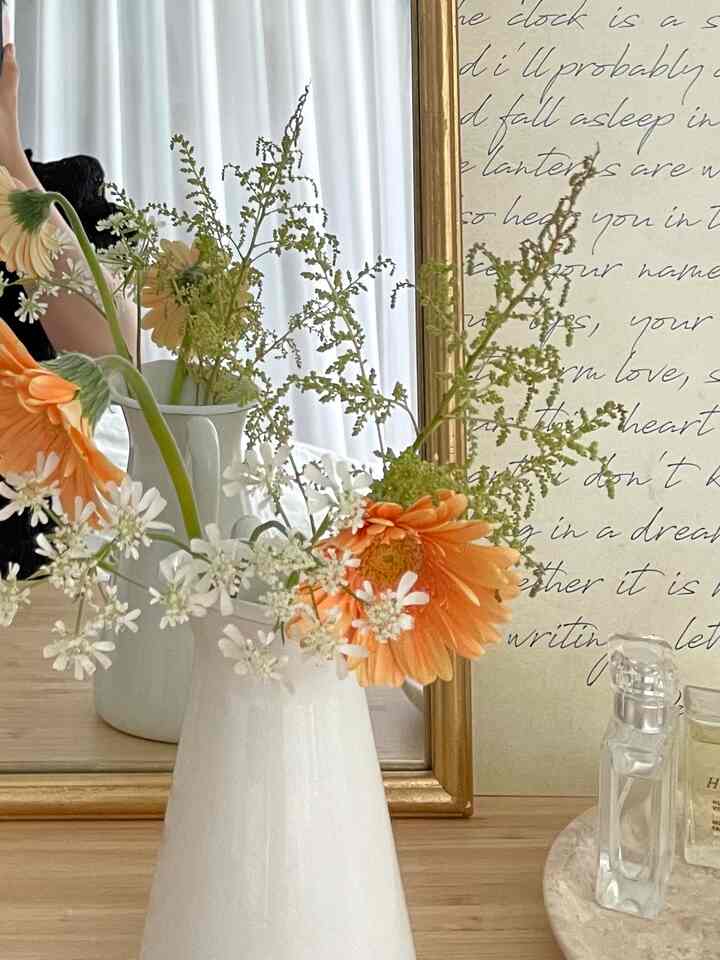 White and gold toned vanity featuring a vase of flowers and a mirror, creating a vintage-inspired bedroom interior