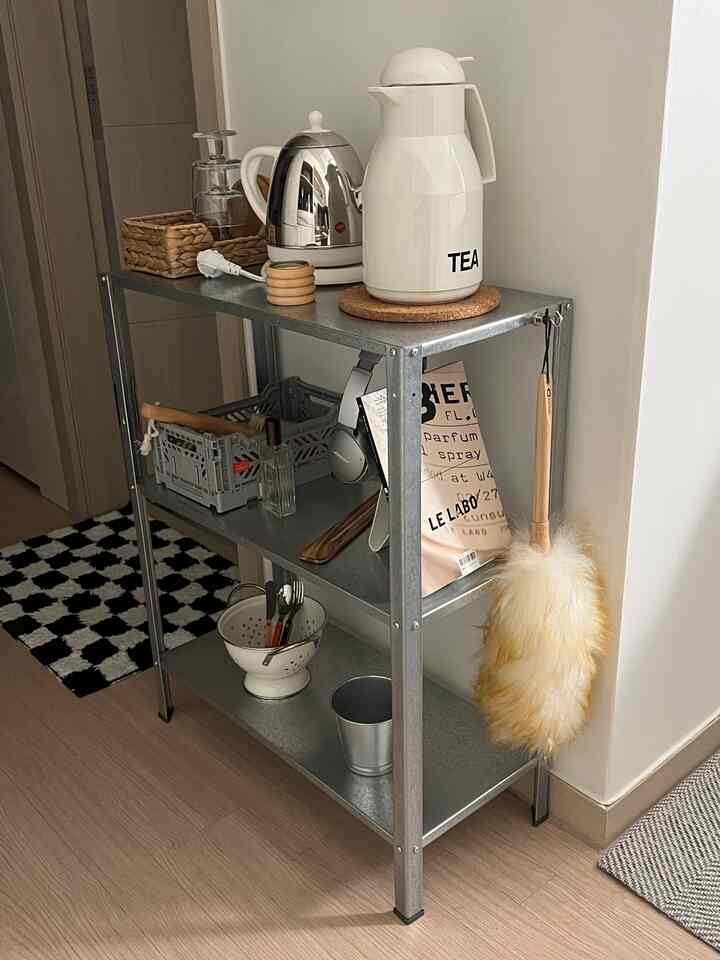 グレーのトーンと木目調の床が調和するワンルームキッチン、イケアの金属製棚とキッチン用品が配置された印象的なインダストリアルでモダンな空間。