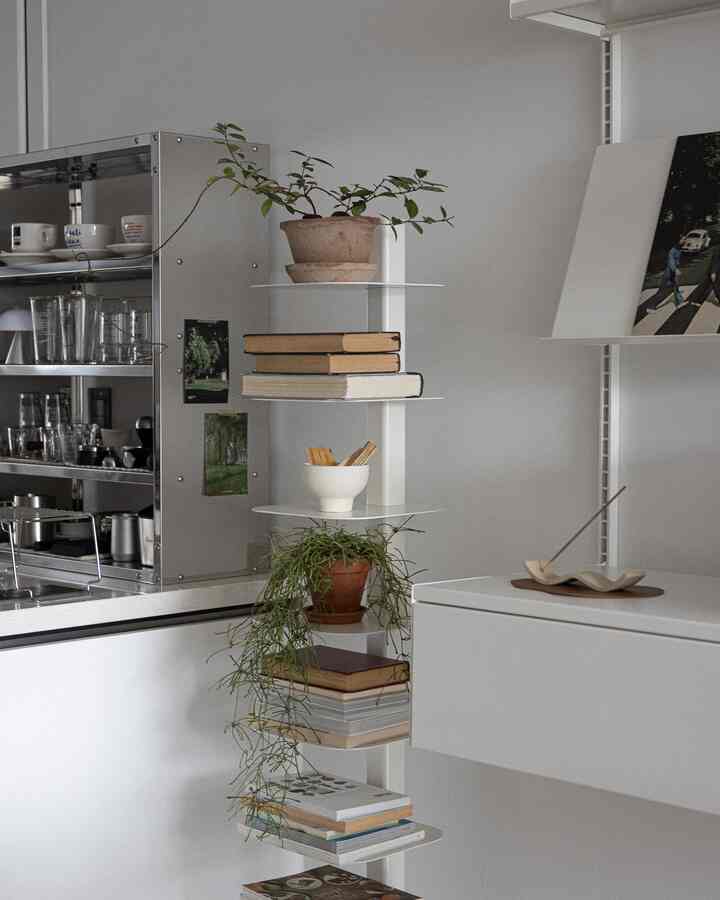 白とナチュラルな色調のキッチンスペース、複数の植物と本が棚に整然と並べられたモダンでミニマルな雰囲気のインテリア