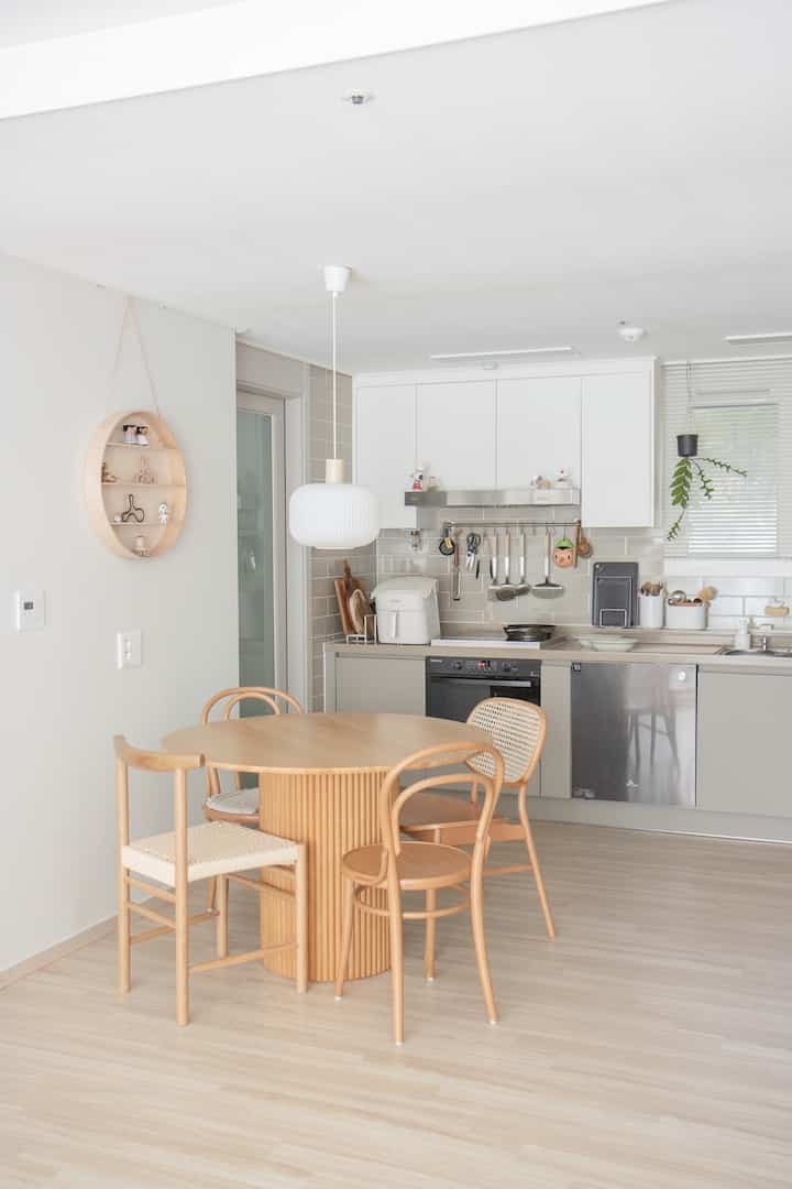Natural kitchen with white walls and ceiling, featuring a light brown wooden round dining table and chairs