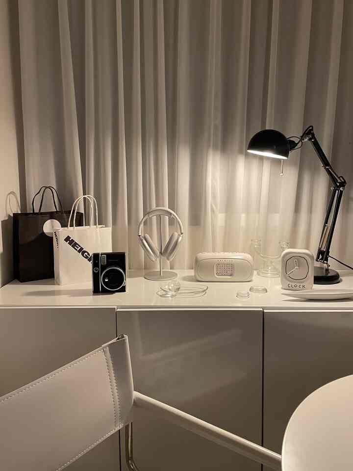 White and monotone living room or home office space featuring white cabinet with decorative items and black desk lamp in a minimal interior