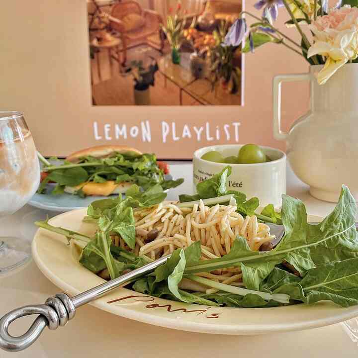 ナチュラルカラーのホームカフェ風ダイニングテーブル、新鮮な野菜とパスタ、ヴィンテージのオブジェ花瓶が配置された雰囲気のあるインテリア