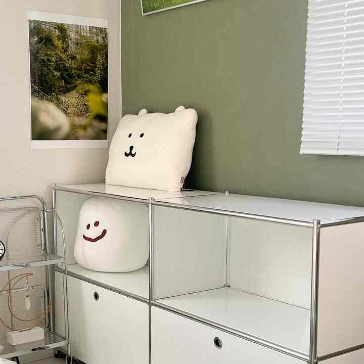 Simple space with white cabinetry and natural green wall, featuring plush cushions and metal shelving