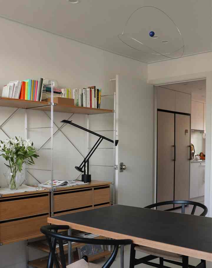 Modern living room with white walls and natural wood shelves, featuring a black desk and office chairs in a neat arrangement