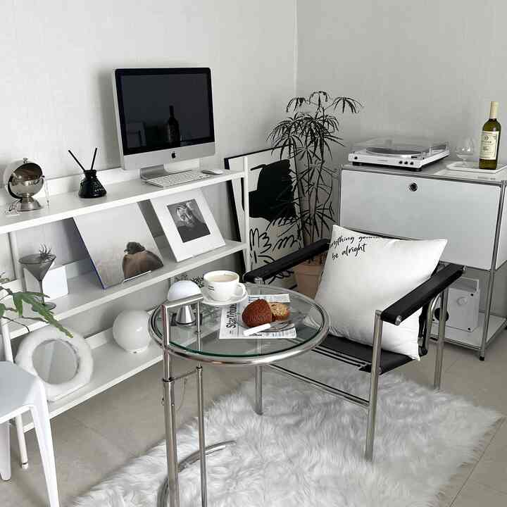 ホワイトとグレーの色調のリビング、丸いガラステーブルと黒い椅子、ミニマルな棚やターンテーブルが配された落ち着いた雰囲気のインテリア