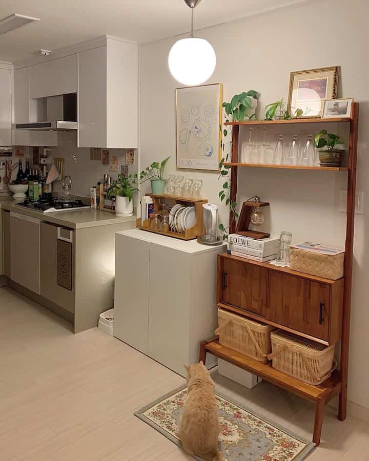 白と木目調が基調のキッチン、植物とゴールドの額縁が配置された雰囲気のあるインテリア