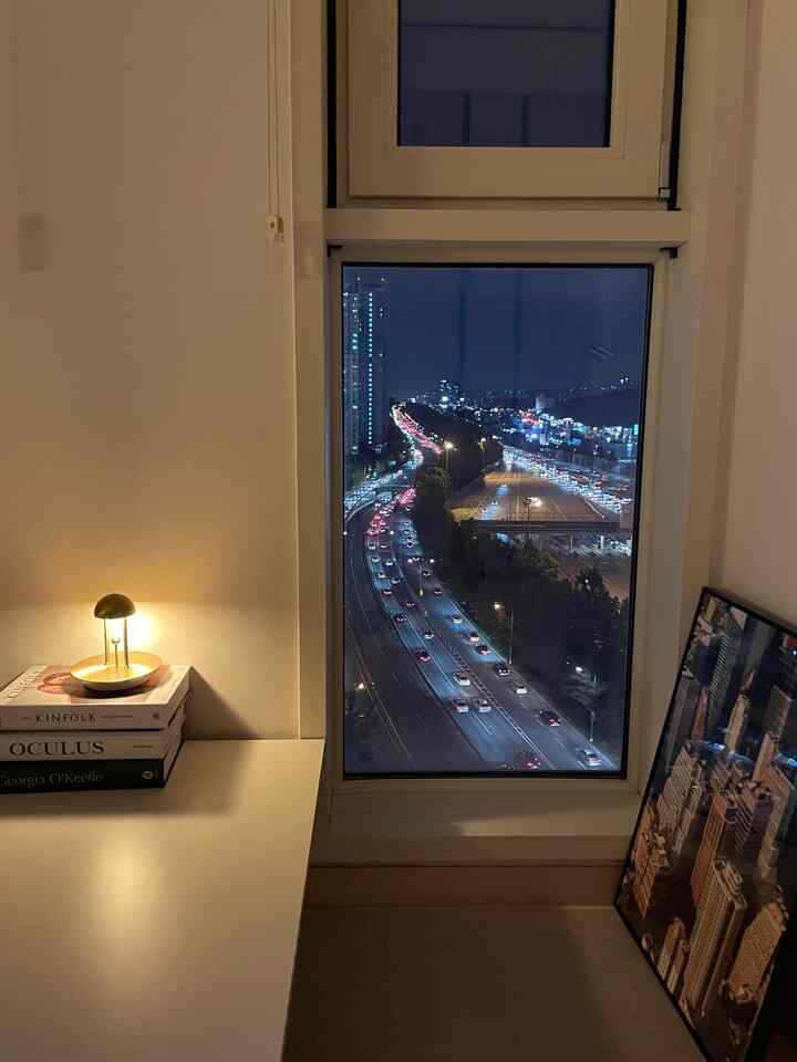 白を基調とした小さなダイニングルーム、窓の外に夜景が見え、テーブルランプとポスターが配置されたシンプルな空間