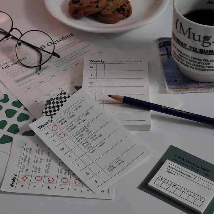 Minimal home cafe setup on a white table featuring memo pads, pencil, and a coffee mug