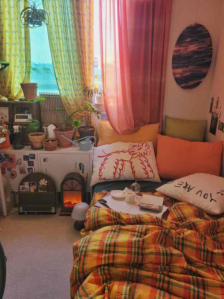 Cozy bedroom featuring warm yellow and pink curtains, assorted cushions, and plants creating a relaxed atmosphere