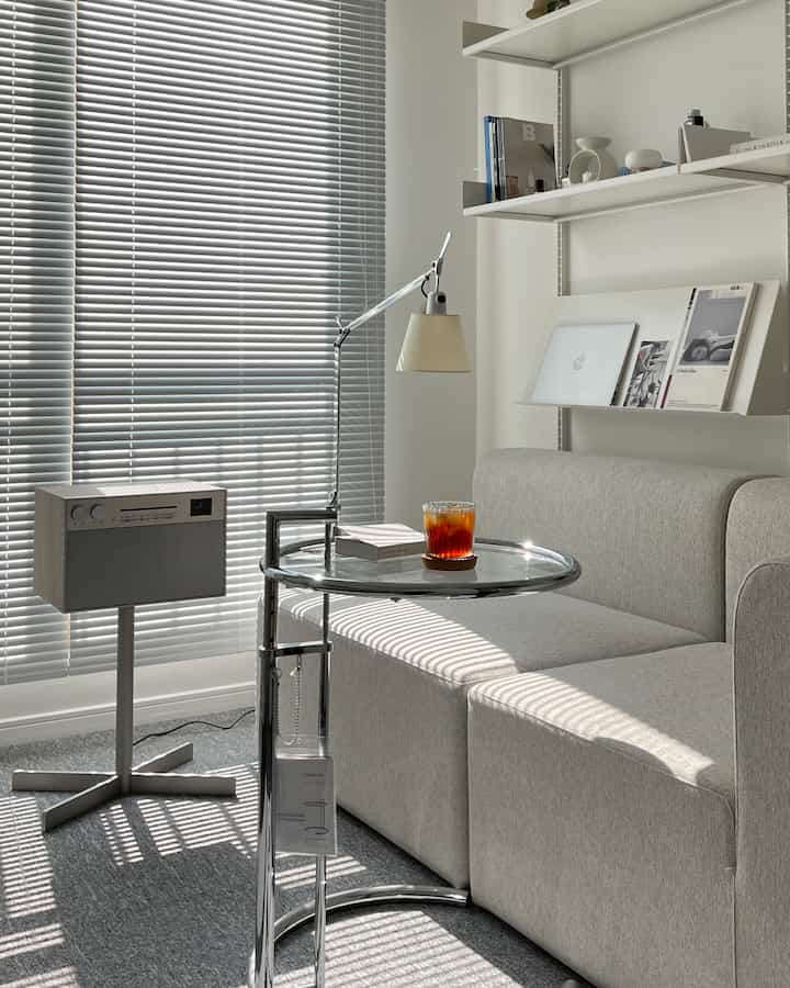 Bright and calm gray and white toned home office space featuring sleek sofa and chrome side table in a cozy study
