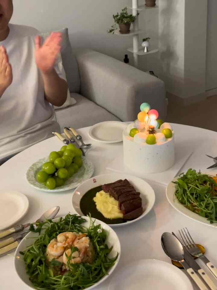 White-toned living dining room featuring a round dining table with assorted dishes and a cake, creating a cozy home party atmosphere