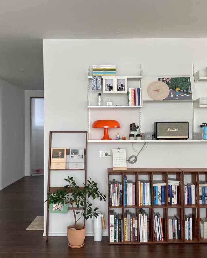 A white and brown toned living room featuring wooden bookshelves and wall shelves with various decor, creating a neat and modern space