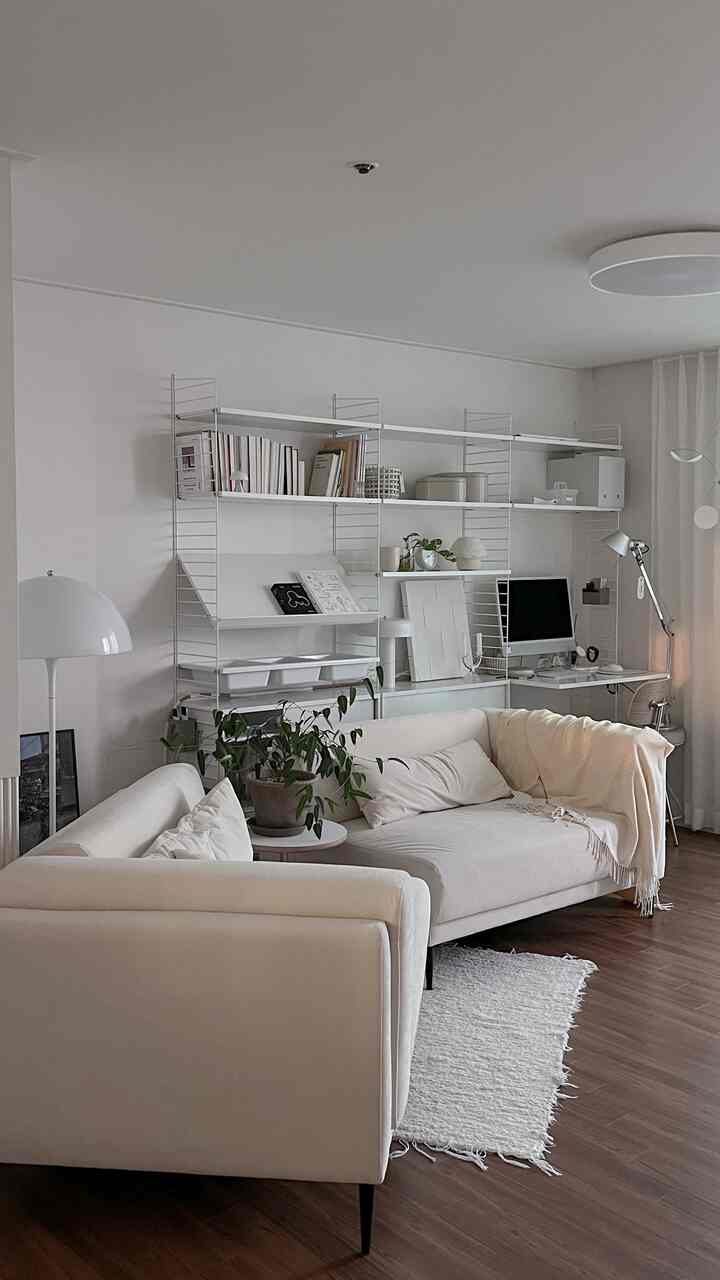 A cozy living room in white and wood tones featuring two sofas, a desk, and plants, blending home office and relaxation areas
