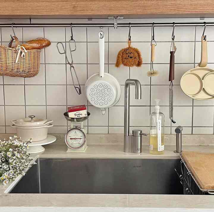 Natural-toned kitchen with white tiled wall and stainless steel sink, neatly organized cooking utensils and cleaning items arranged