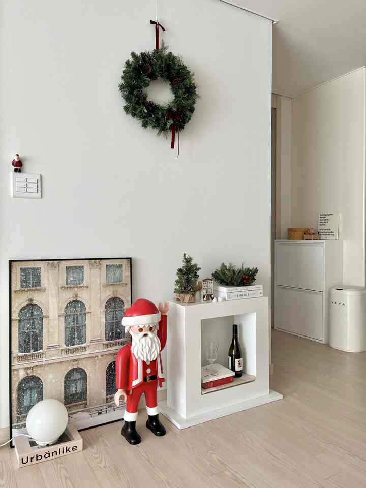 White-toned living room corner featuring Christmas-themed decorations and a red Santa objet with a cozy atmosphere