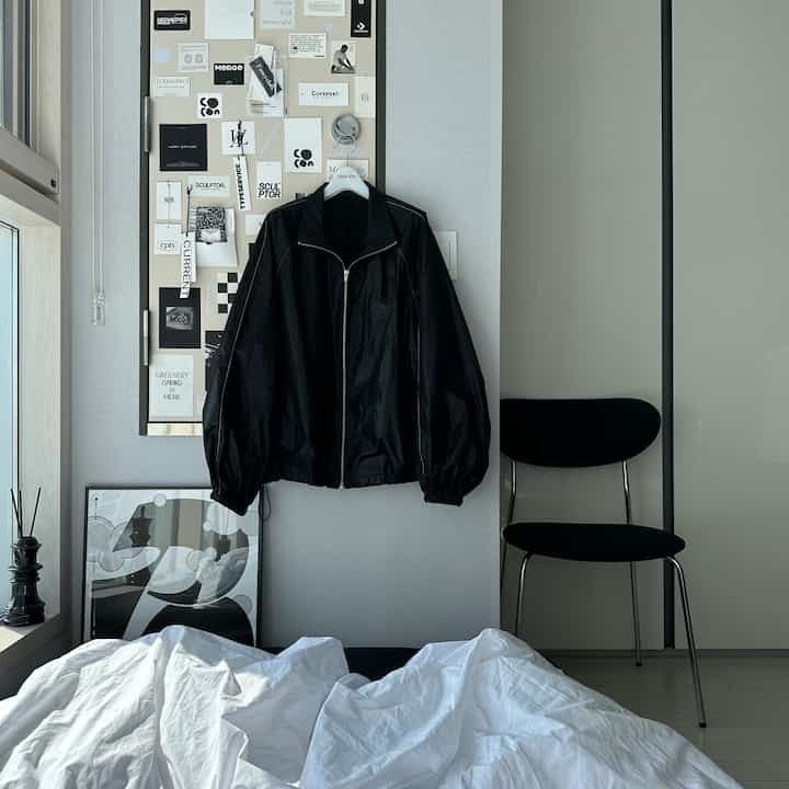 モノトーンの寝室、壁に黒いジャケットと額縁が飾られたシンプルで雰囲気のあるインテリア