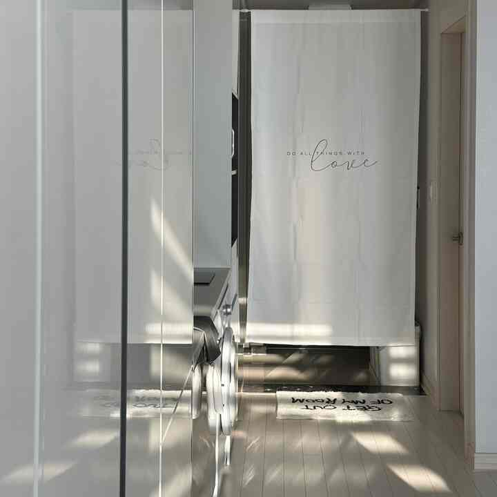 Monotone white and gray narrow entrance space featuring a washing machine and entrance curtain in a clean modern interior