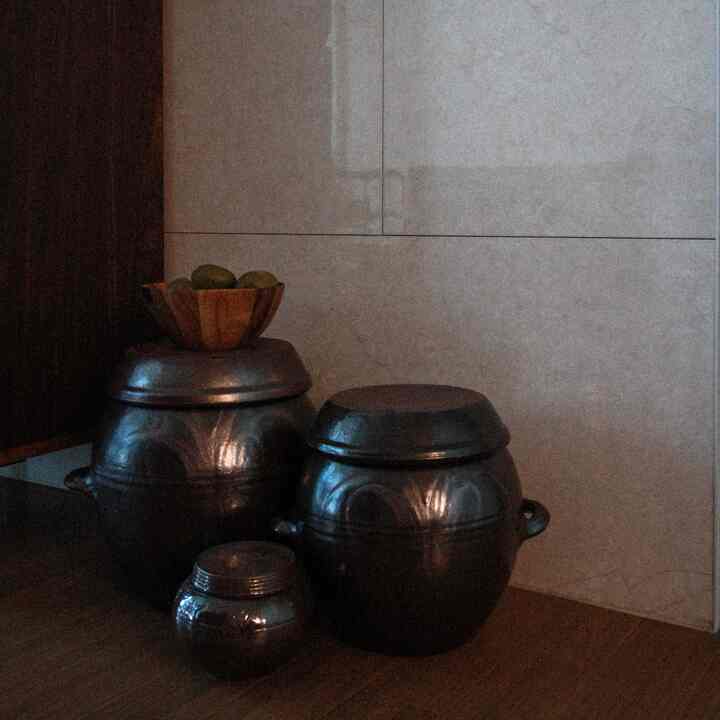 暗いダークブラウンの醤缶台が木の床と明るい壁の前に集まった、韓国風の静かなインテリア