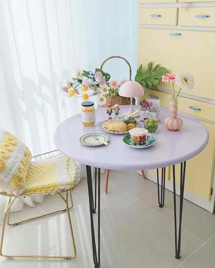 Yellow cabinets and white curtains frame a dining space with a round table featuring flowers and cute accessories, creating a cozy home cafe vibe