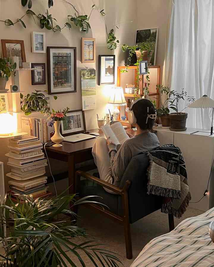 ナチュラルな色調の居心地の良いリビングルームのホームオフィス、アームチェアとデスクの周りに額縁と植物が配置された落ち着いた読書空間