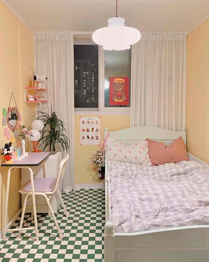 Yellow-walled kids' bedroom with green checkered flooring, heart-pattern pillows, and teddy bear posters creating a cozy atmosphere