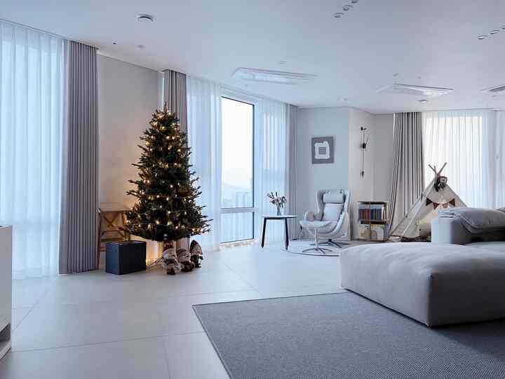 ナチュラルカラーの変形間取りリビング、大きなソファとアームチェア、コーナー収納、プレイテントが配置された印象的なモダン空間