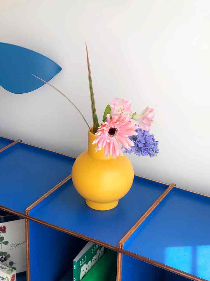 A modern space with bright white walls and deep blue shelves featuring a yellow vase with pink and purple flowers