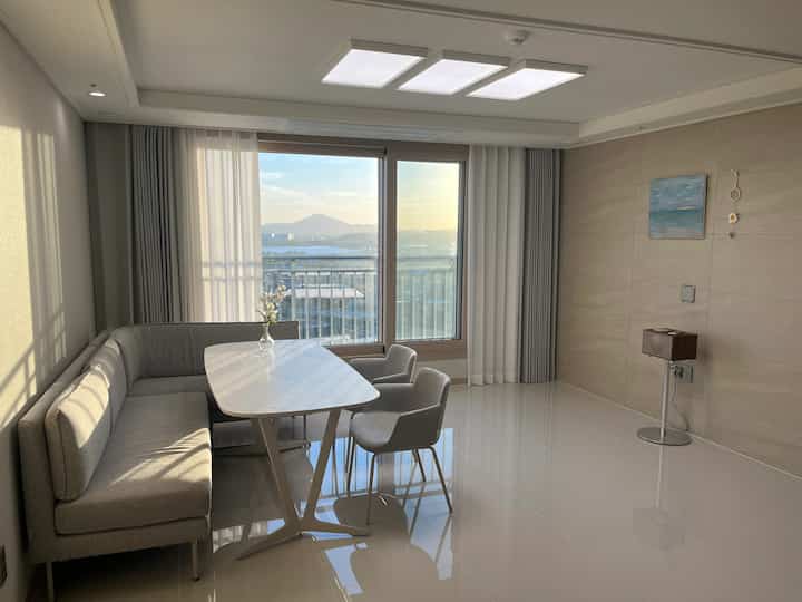 ベージュ調のリビング・ダイニングルーム、大きな窓からハン川の眺めが見え、ミニマルで清潔感のあるインテリア