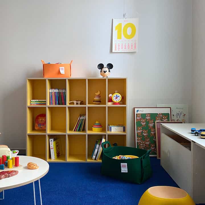Playroom with blue rug and yellow bookshelf featuring toys and children’s books, creating a cozy organized area for kids