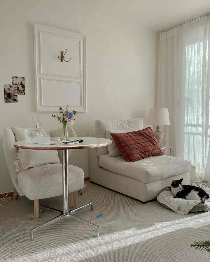 柔らかなホワイトとベージュのリビング、一人用ソファとアームチェア、チェック柄クッションと猫がいる温かみのある空間