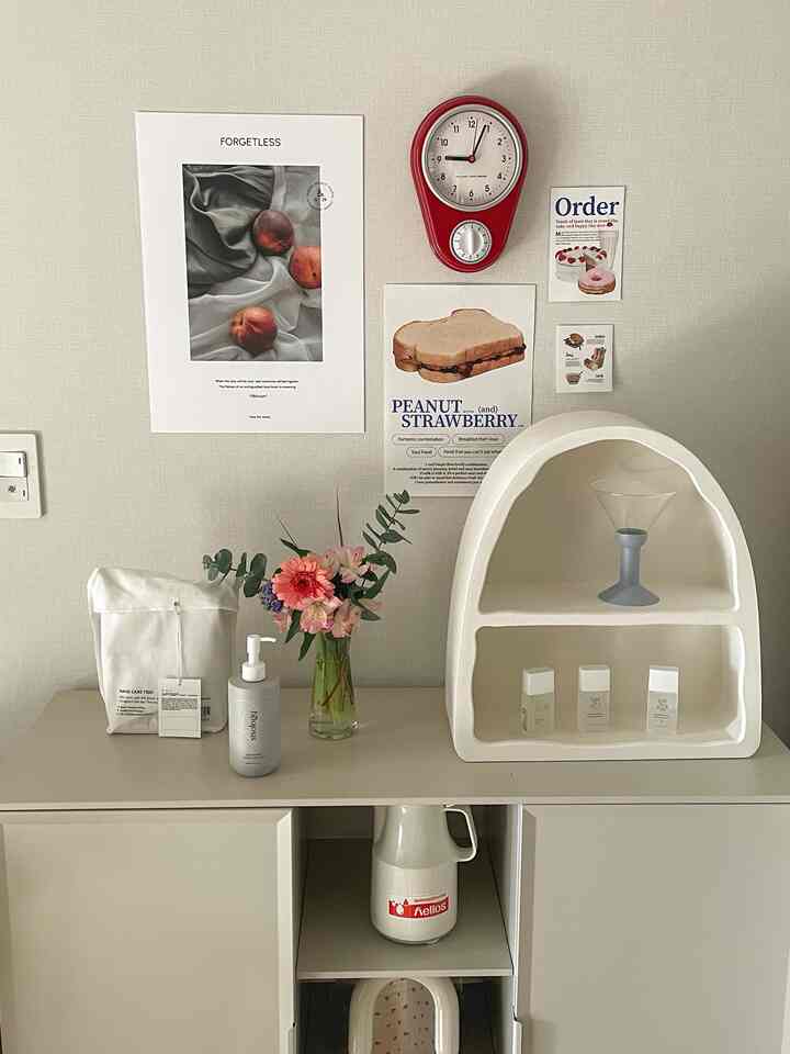 Minimal kitchen space with white walls and shelves, featuring a red clock, vase of flowers, and wall art for a clean look