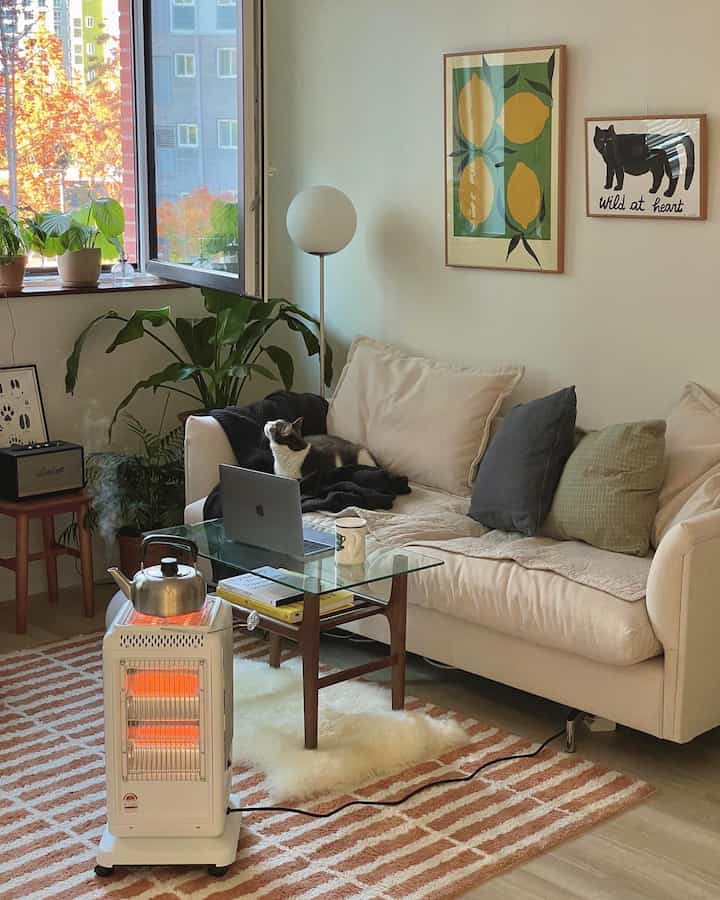 Natural beige-toned living room featuring a beige sofa with a cat, Obang heater, and floor lamp creating a cozy atmosphere