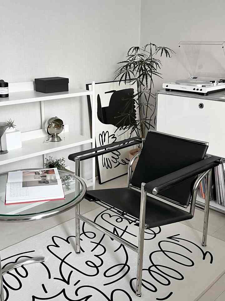 Modern home office space in white and black tones, featuring a black leather chair, glass table, and artistic rug in a clean interior