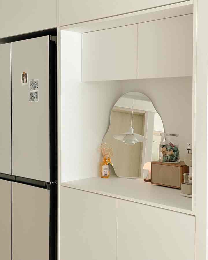 White-toned kitchen space featuring an irregular mirror and coffee capsule machine, arranged in a modern and minimal style with a clean look